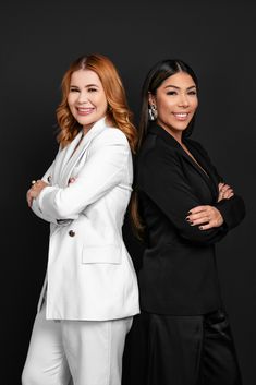 two women standing next to each other in front of a black background with their arms crossed