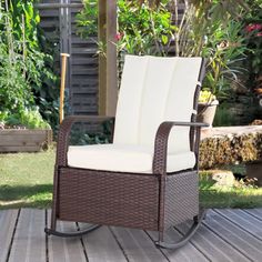 an outdoor rocking chair with white cushions on a deck in front of some plants and flowers