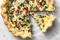 a quiche with spinach, bacon and cheese on top is cut into slices