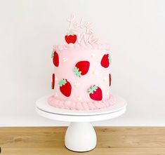 a pink cake with strawberrys on it sitting on top of a table