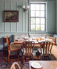 a dining room with blue walls and wooden tables set for four, along with white plates and glasses on the table