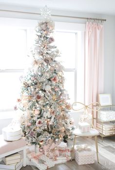 a white christmas tree with pink and gold ornaments in a living room setting, surrounded by presents