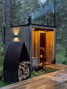 a small cabin in the woods with a firewood log and an open door to it