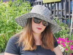 a woman wearing a hat and sunglasses sitting on a bench in front of some flowers