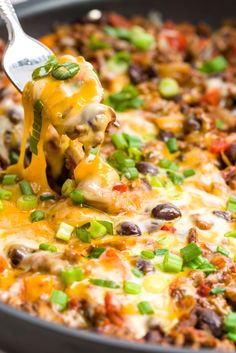 a spatula scooping some food out of a skillet with cheese and black beans