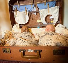 two baby dolls are laying in an open suitcase with clothes hanging on the clothesline