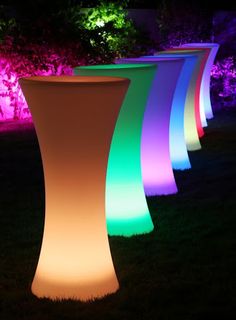 illuminated vases in the grass at night with colored lights on them and trees in the background