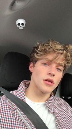 a young man sitting in the back seat of a car with a skull hanging from the ceiling