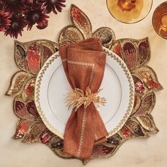 a place setting with napkins, flowers and candles on a table cloth covered plate