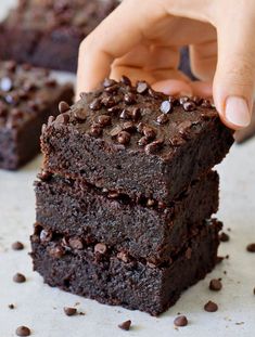 a hand picking up a piece of chocolate brownie from the stack on top of each other