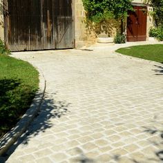 a brick driveway leading to a garage with an open door and green grass in the foreground