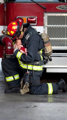 a fireman holding a baby in front of a firetruck with his head on the ground