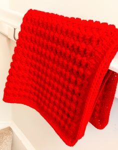 a red crocheted blanket hanging from a hook on a white door handle,