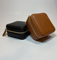 two small black and brown cases sitting next to each other on a white surface with gold zippers