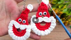 two crocheted santa clause earrings being worked on by a person holding a pair of scissors