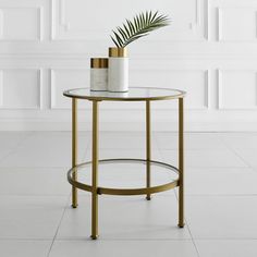 a round glass table with a plant on top in front of a white wall and floor