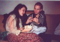 a man and woman sitting on a couch looking at something in their hands as they talk to each other