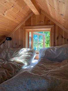 two beds in a small room with wooden walls and ceilings, one has a window on the other side