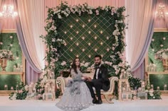 a bride and groom sitting on a chair in front of a floral backdrop