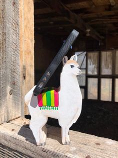 a llama figurine with a colorful scarf on it's back sitting on a piece of wood