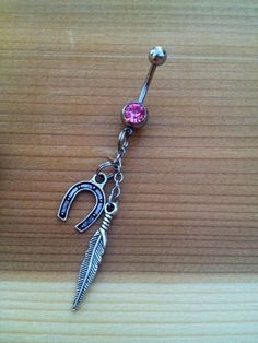 a pink jeweled belly ring with an arrow and feather dangling from it's side