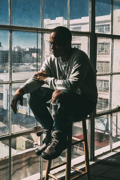 a man sitting on top of a wooden stool next to a window