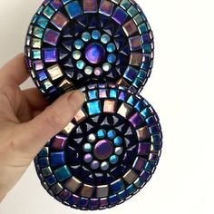 a hand is holding two small pieces of colorful glass mosaics on a white surface