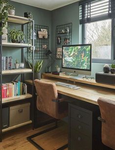 a desk with a computer and bookshelves in front of a window filled with plants