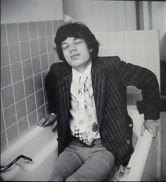 a man sitting on top of a bath tub next to a white tiled bathroom wall