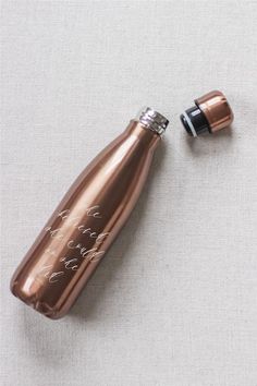 a copper colored water bottle sitting on top of a white surface next to a black and silver cap