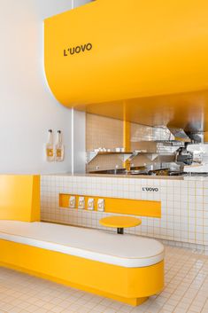 the interior of a restaurant with yellow and white furniture, including a long bench that sits in front of an oven