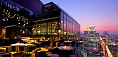 an outdoor restaurant overlooking the city at night with lots of tables and chairs on it