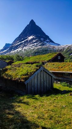 an old barn with grass on the roof and mountains in the background