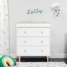 a baby's room with a white dresser and green toy car on the floor