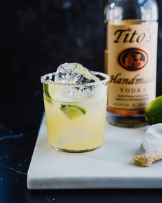 an alcoholic drink with ice and lime on a white plate next to a bottle of booze