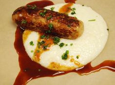 there is a sausage on top of some mashed potatoes with sauce and chives