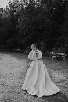 a black and white photo of a woman in a wedding dress standing on the grass