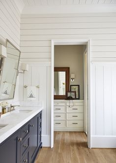 a bathroom with white and blue cabinets and wood flooring on the walls, along with a large mirror over the sink