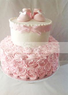 a pink cake with two baby shoes on top