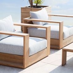 two wooden chairs sitting next to each other on top of a tile covered floor near a potted plant