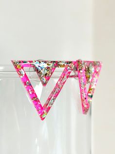 a pair of pink triangle shaped earrings hanging from a glass holder on a white wall