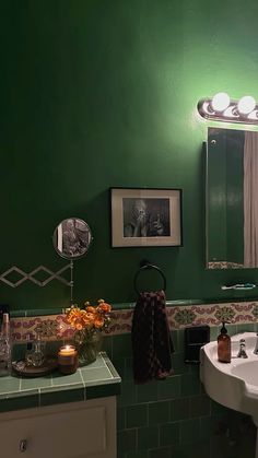 a bathroom with green walls and white sink, lights above the mirror and pictures on the wall