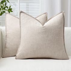 two pillows sitting on top of a white couch next to a potted plant in front of a window