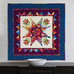 a white bowl sitting on top of a wooden table next to a wall mounted quilt