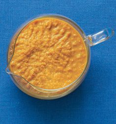 a small glass bowl filled with yellow colored food on a blue surface next to a spoon