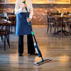 a man standing in a restaurant holding a green and black cleaning mop on top of a hard wood floor