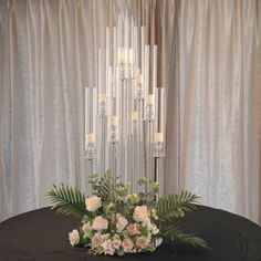 a centerpiece with candles and flowers on a table in front of curtained backdrop