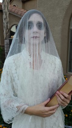 a woman dressed in white is holding a box and wearing a veil with her eyes closed