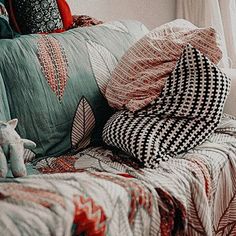 a bed covered in pillows and blankets next to a window