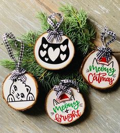 four decorated christmas ornaments on top of a wooden table with pine needles and plaid ribbon